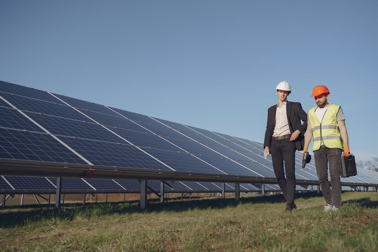 contact-img Full body of young focused manager in formal wear and electrical technician in uniform walking on path near solar panels and discussing working process