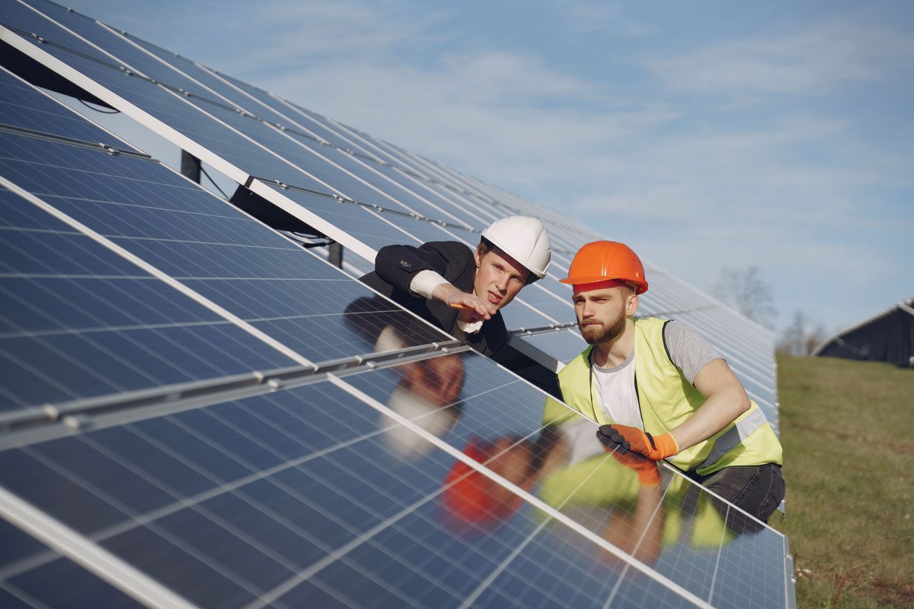 why-choose-us Concentrated male coworkers in hardhats working at solar energy station and discussing technical aspects of panels
