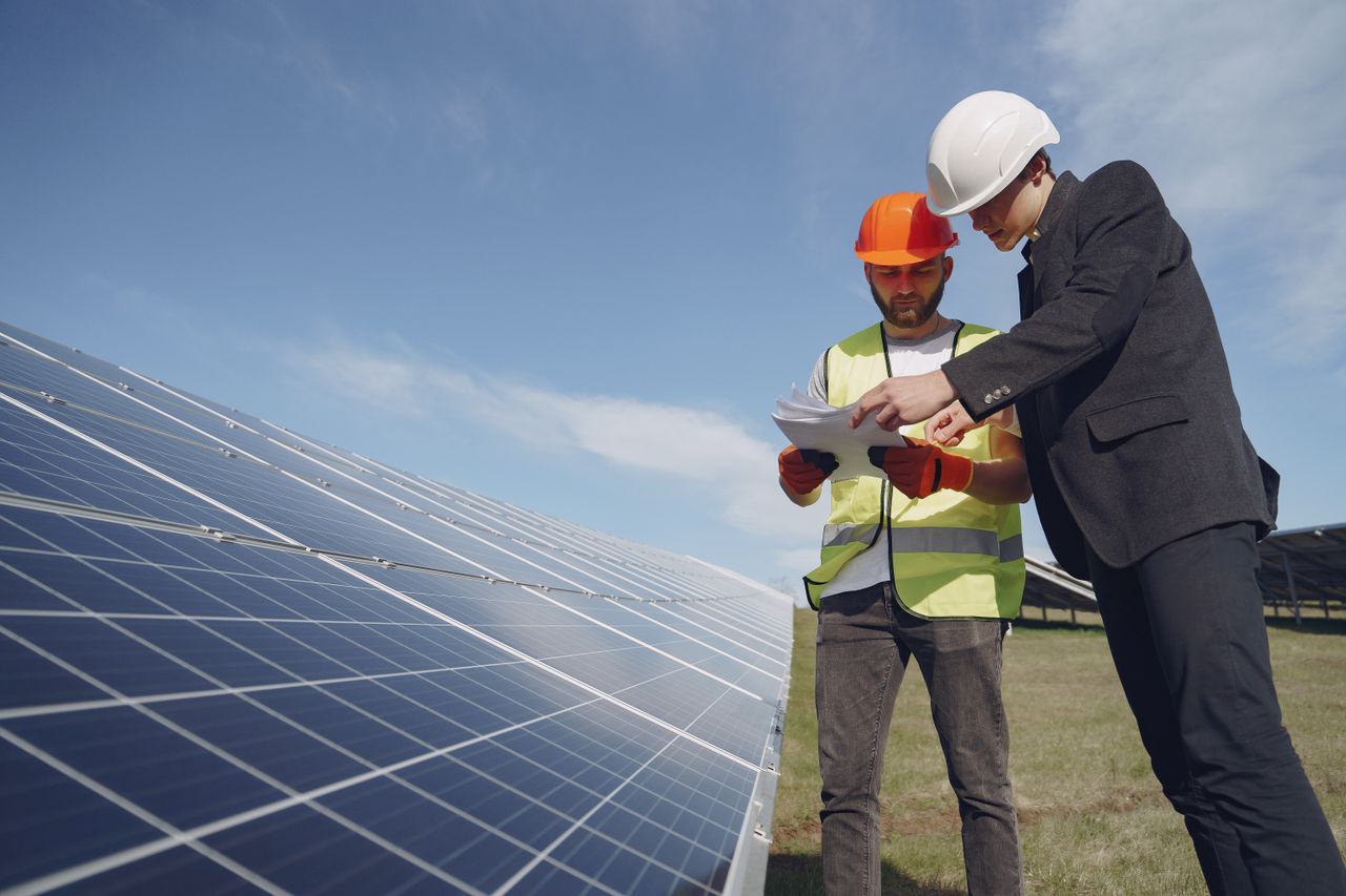 our-experience Low angle of young inspector and foreman in hardhats checking documentation against modern solar panels in field