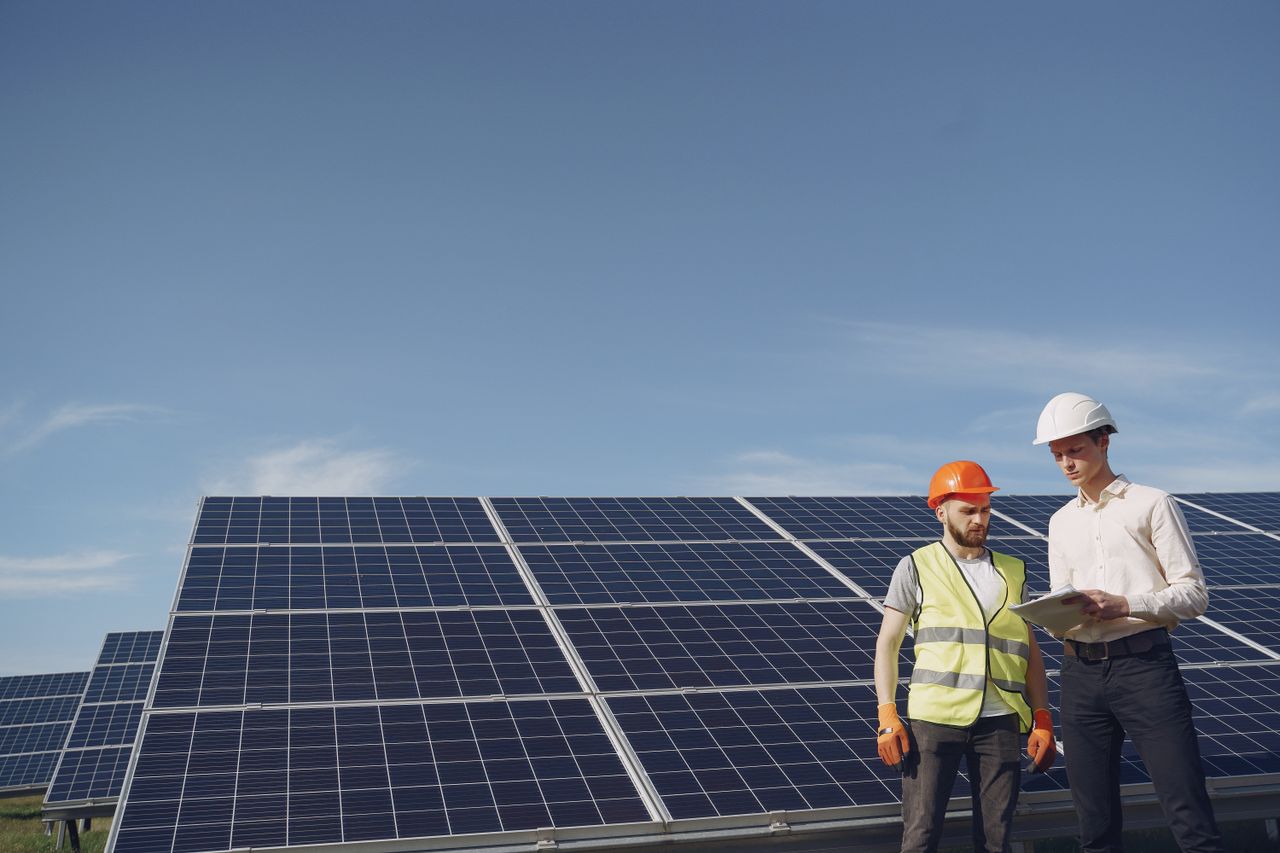 hero-img-02 From below of serious young male colleagues in helmets working at solar energy station against cloudless blue sky