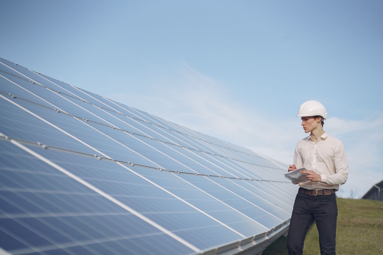 about-01 Young serious male engineer in formal outfit and helmet reporting while inspecting solar panel field