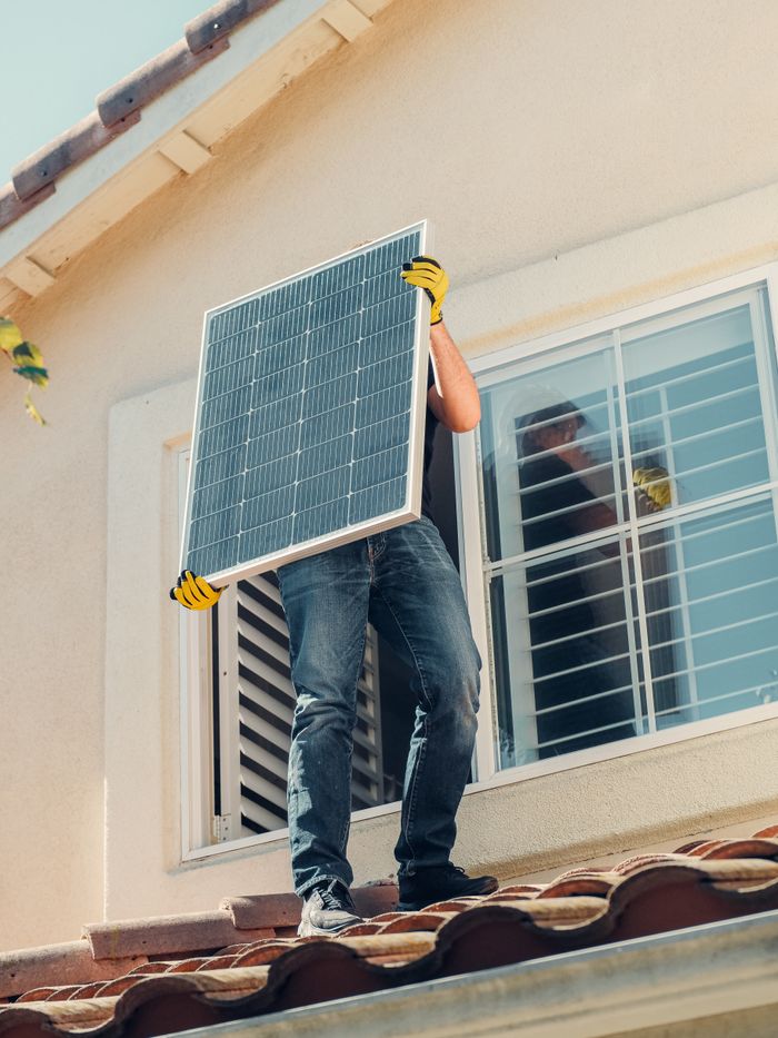 gallery-3 Technician carrying a solar panel on a rooftop for installation, promoting renewable energy.