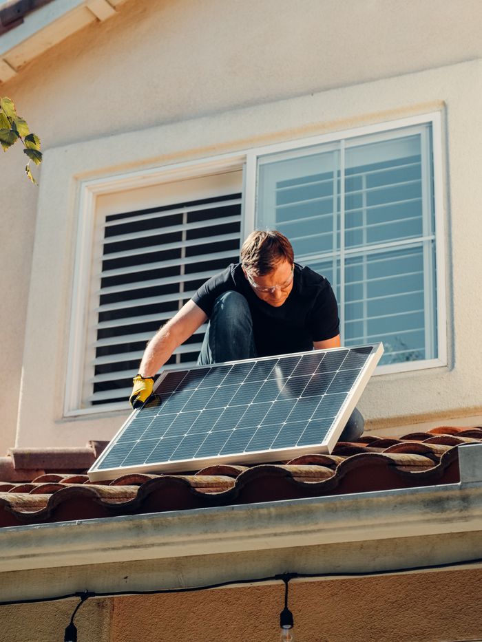 gallery-1 A worker installing a solar panel on a residential rooftop under bright sunlight.