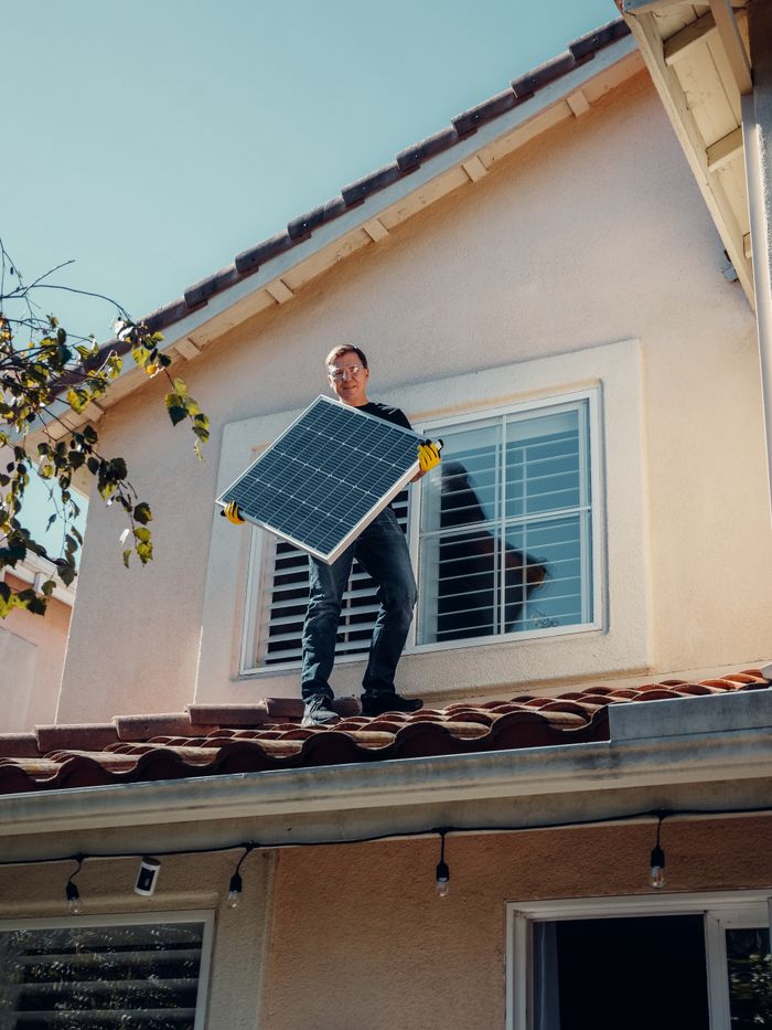 services-03 An adult male worker installing a solar panel on a house roof, showcasing clean energy in action.